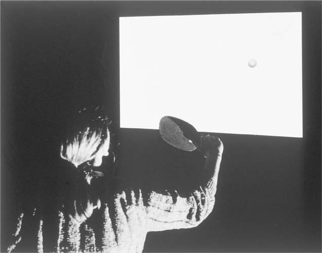 A photograph of a man playing ping pong against the screen. He holds a paddle and the ball is seen on the screen.