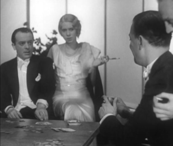 Two elegantly dressed men sit opposite each other as they play cards. A woman in white, holding a long cigarette, sits on one of their armchairs.