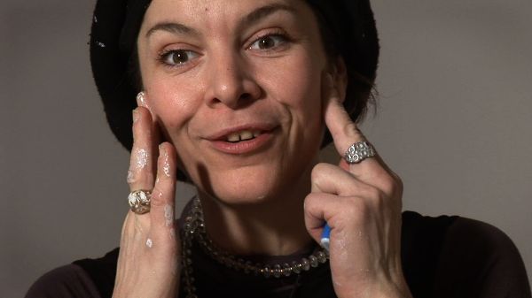 A woman smiling with both hands touching her cheeks emphasizing the smile, as if teaching someone how to smile.
