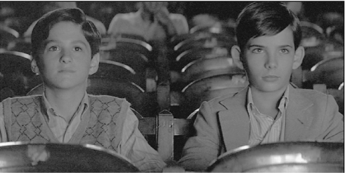 The exhibit displays a scene from the movie “Bad Education,” featuring a front view of two young boys dressed formally, sitting in a cinema theatre, captivated by what they are watching, as their expressions indicate.