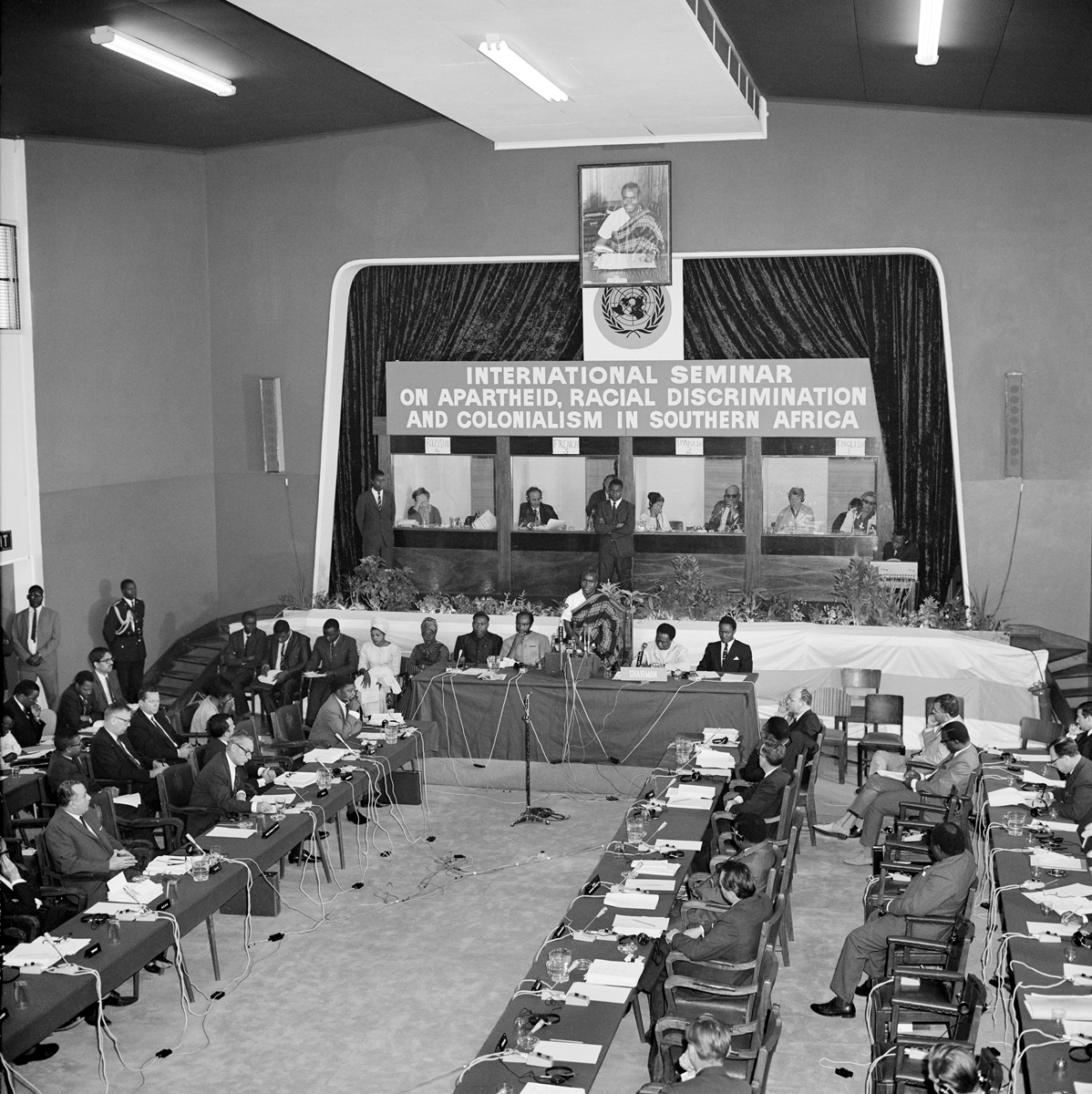 Photograph of delegates seated at desks parallel to walls with simultaneous interpretation booths on the back and a rostrum in front of them.