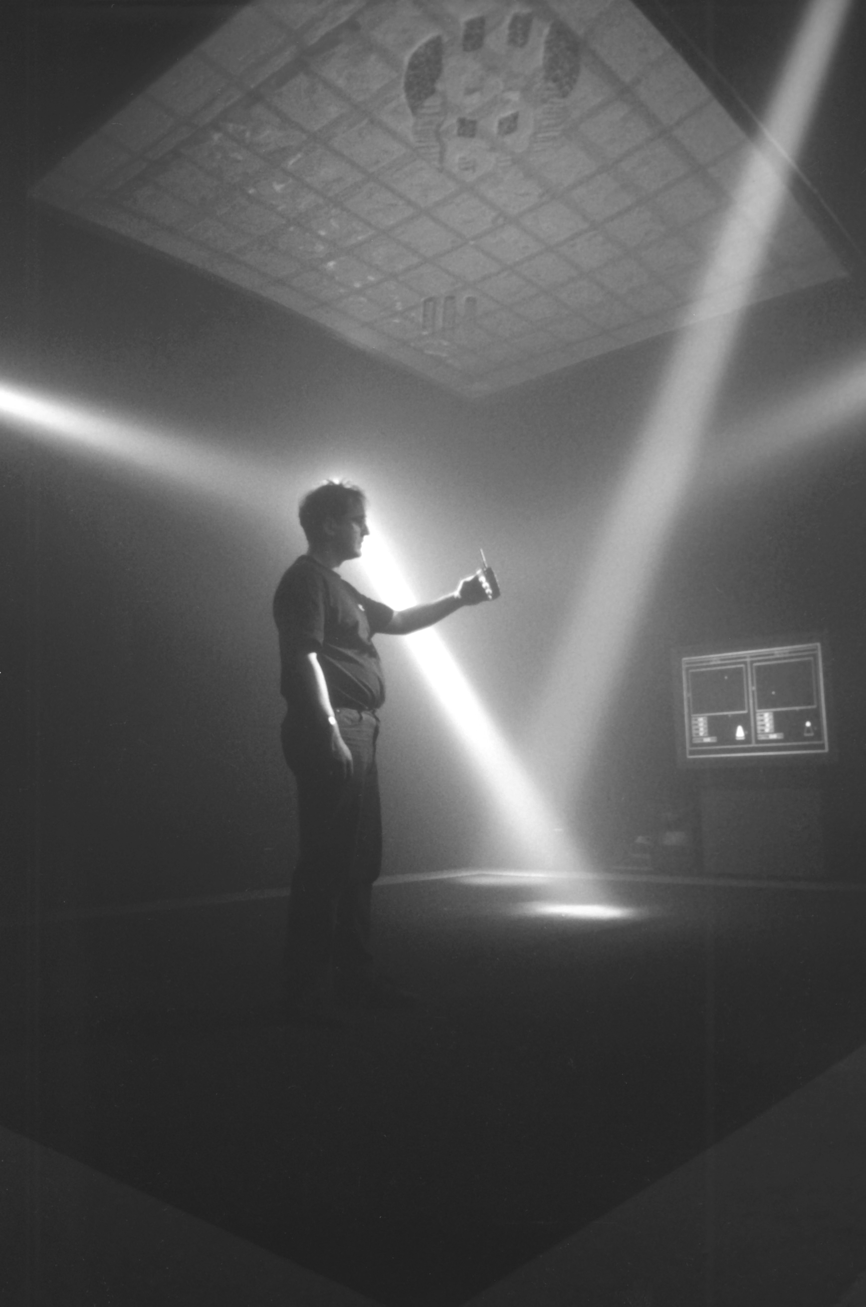 Installation of The Trace showing a man standing in a dramatically lit room interacting with the installation. Projections visible on the ceiling.