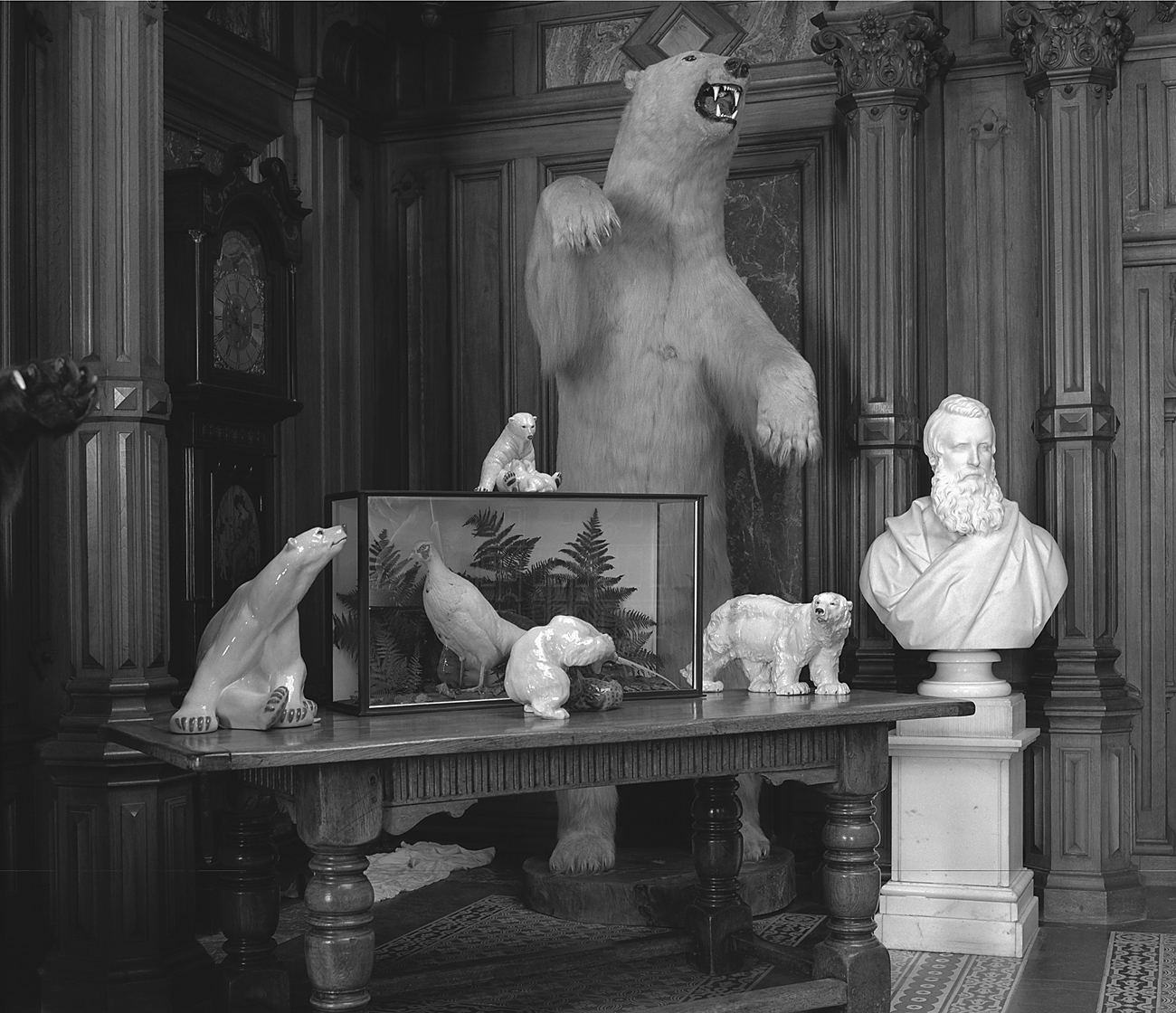 A room with a taxidermy polar bear, porcelain animal figurines, a glass display case, and a marble bust on a wooden table.