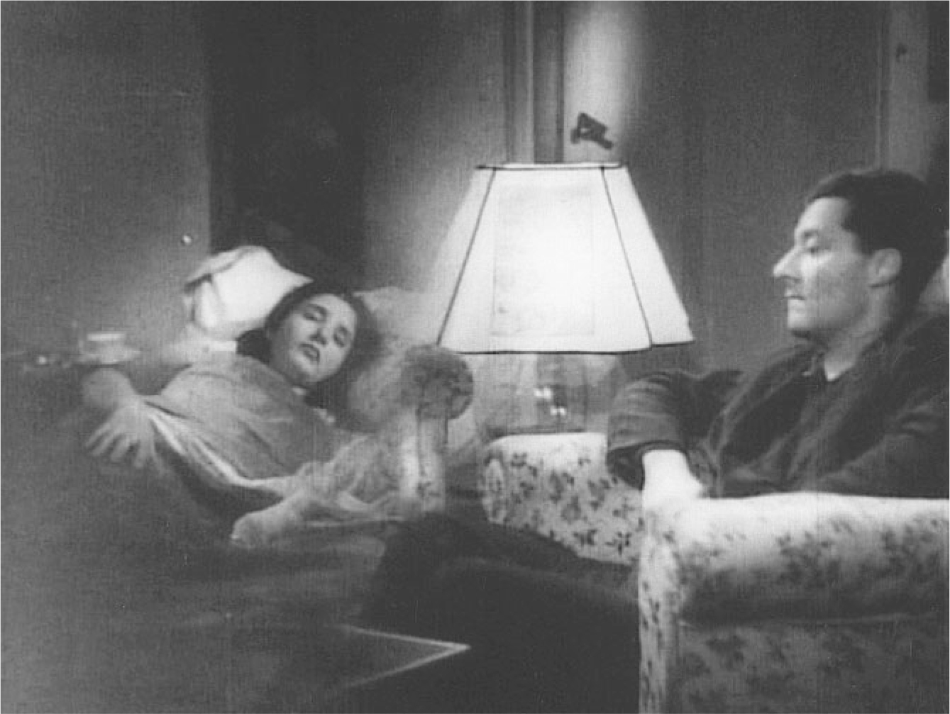 The exhibit depicts a scene from the movie “Roma, città aperta” where a woman is lying on a bed, and a man is seated in a chair next to her. In the vicinity of the bed, there is a large lamp.