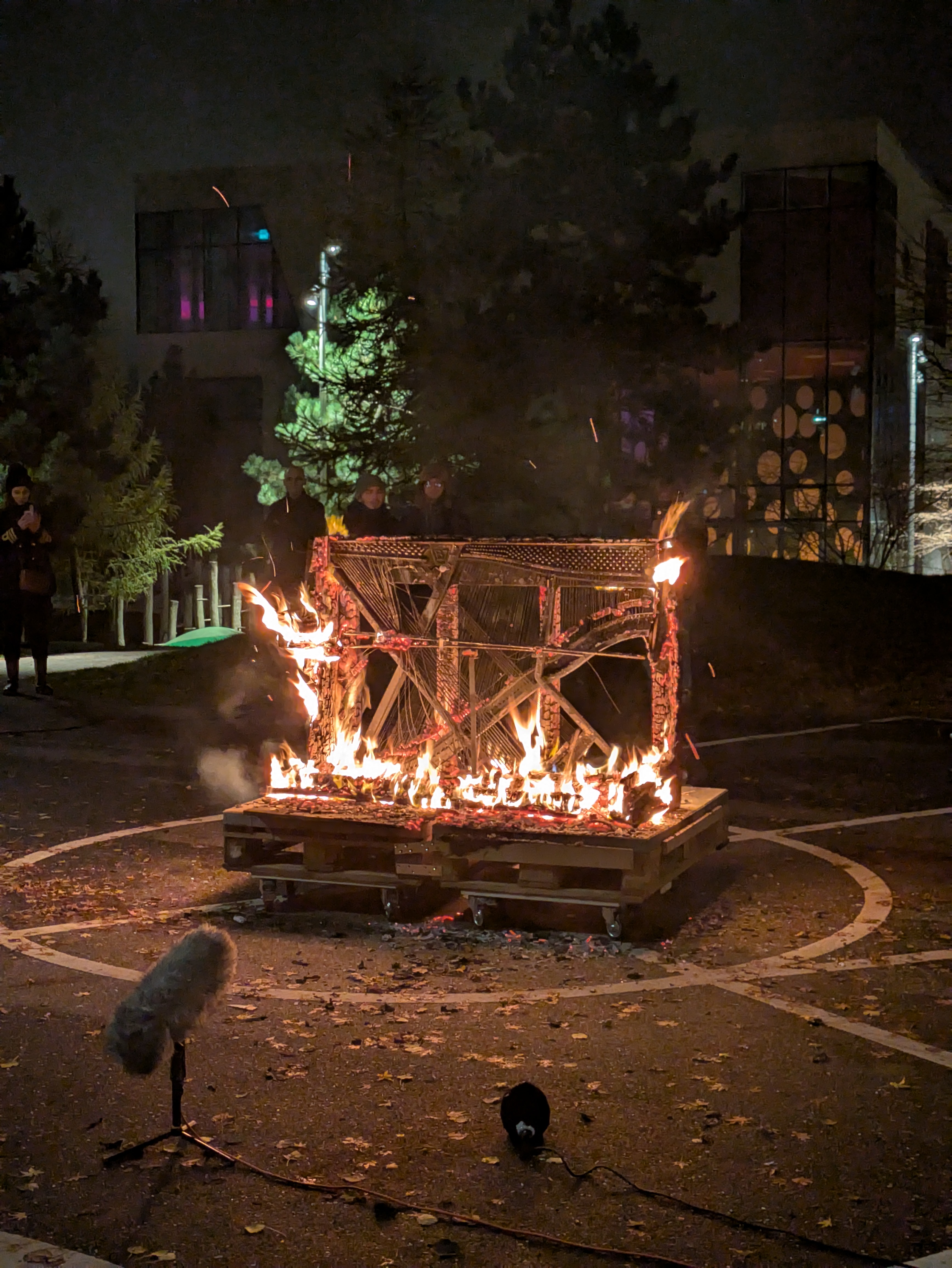 A burning upright piano with the inner harp exposed and a microphone facing the instrument.