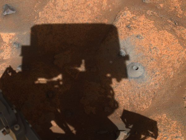 A photograph taken by the Mars Perseverence robot of Mars’s surface, including the shadow of the robot itself.