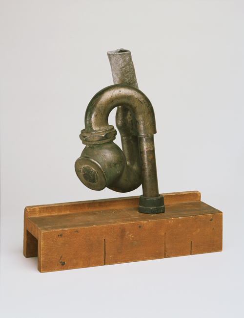 The exhibit displays a wood miter box and a cast iron plumbing trap.
