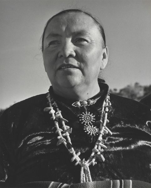 A head shot, from below, of a woman who looks past the camera. Her hair is pulled back and a blanket is just visible wrapped high around her waist.