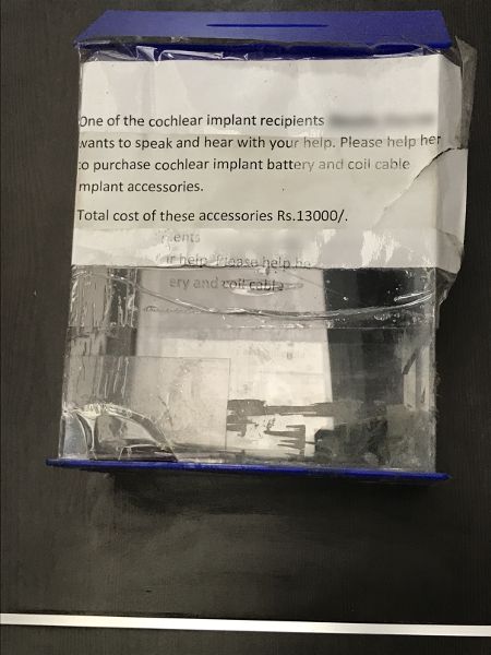 An empty collection box hangs on a wall with a note taped to it.