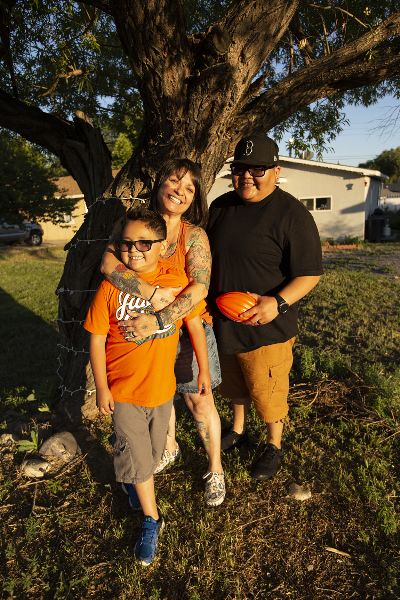 Two women and a child stand beneath a tree obscuring a house.