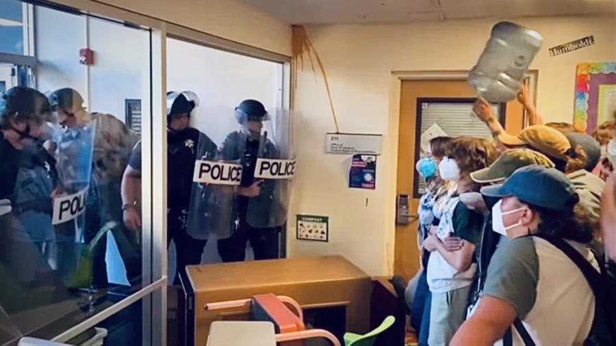Students barriace the entrace of Siemens Hall with desks and chairs from classrooms. Facing of against police officers armed with riot shields, one of the students in the group raises an empty clear plastic water jug to signal their resistence.
