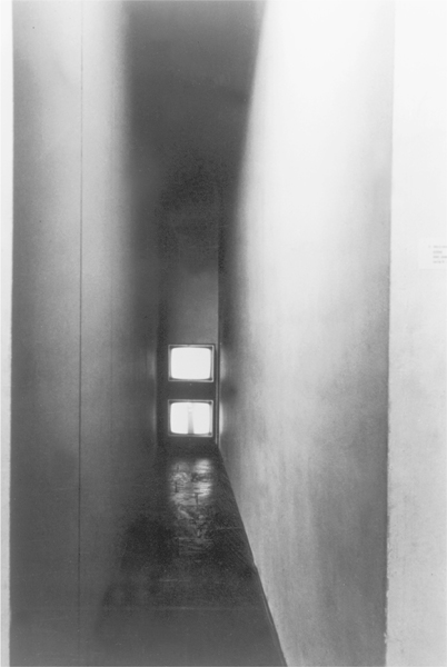 A photograph showing the closed-circuit view camera with 2 televisions at the far end, one below the other mounted in between 2 walls.