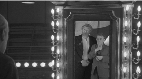 The exhibit portrays the reflections of two men dressed in formal suits on a mirror. The vertical borders of the mirror and the room are illuminated by small bulb lights.