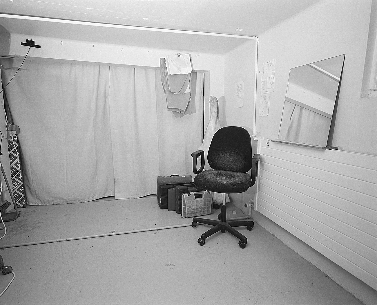 A small room with a swivel chair, a mirror, and various items like boxes and fabric near a curtained area.