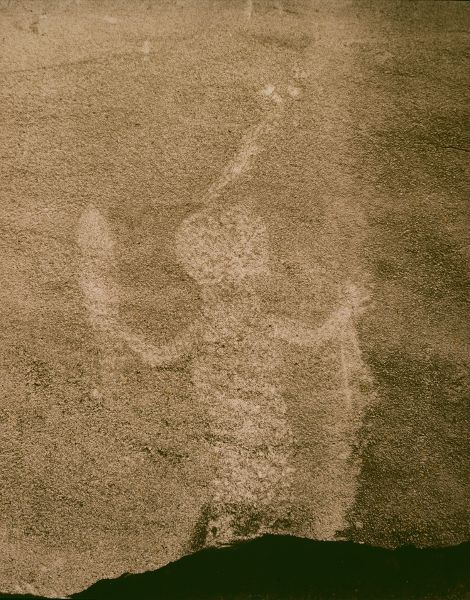 A carving of an anthropomorphic figure with outstretched arms, holding maize.