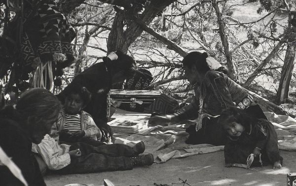 Two adolescent girls look at a binder of photographs by Laura Gilpin; three other children surround them.