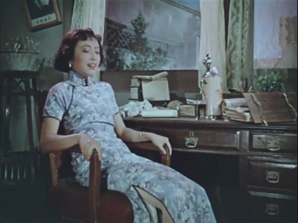 A young woman in floral dress leaning back in a padded wooding chair.
