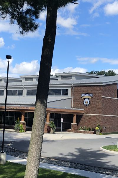 A tree stands in front of a large brick building on a partly cloudy day. A logo on the building says “Nazareth Golden Flyers” above an eagle.