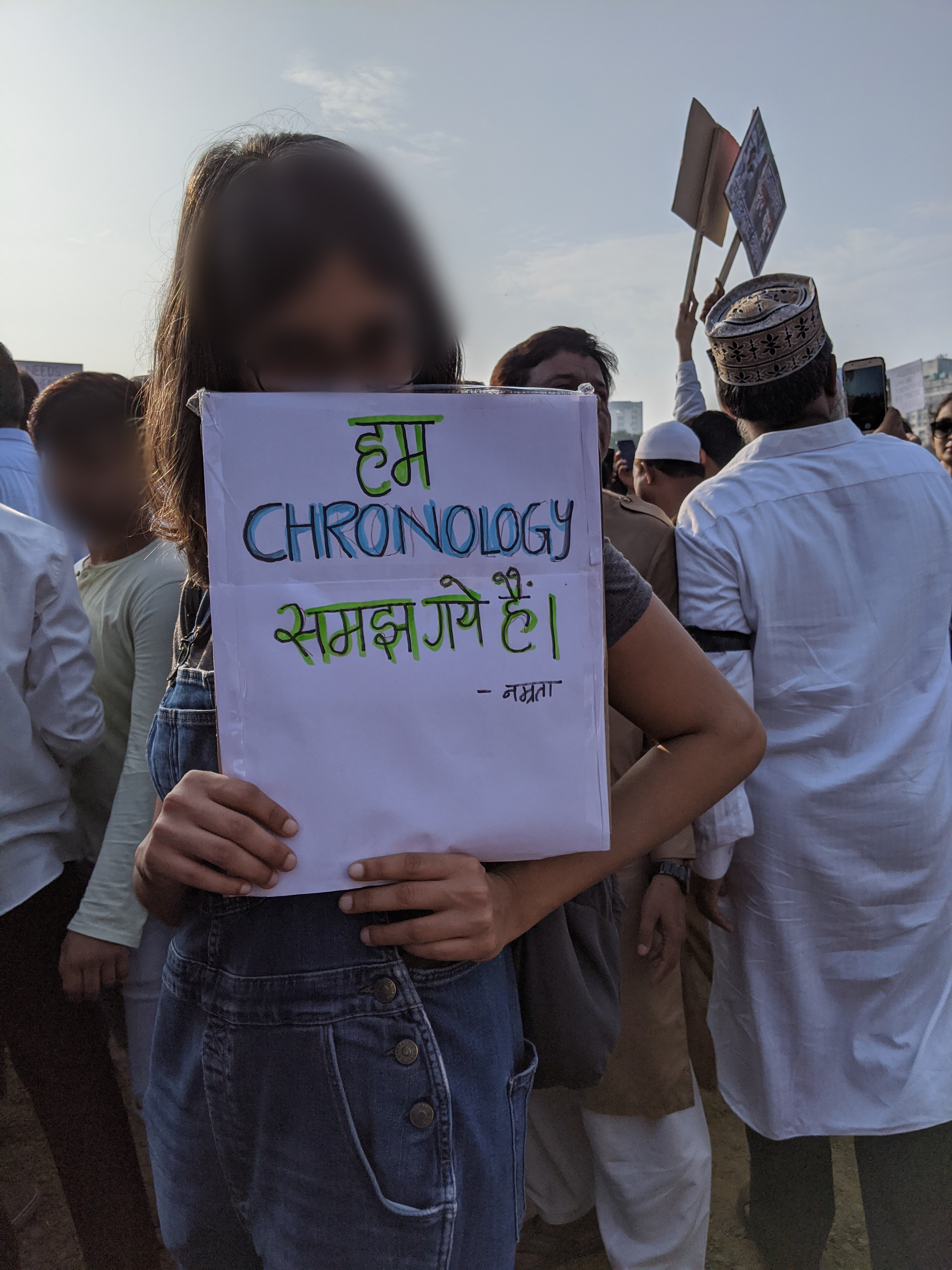 A woman holds a handmade protest sign in front of her face. Other protesters stand behind her.