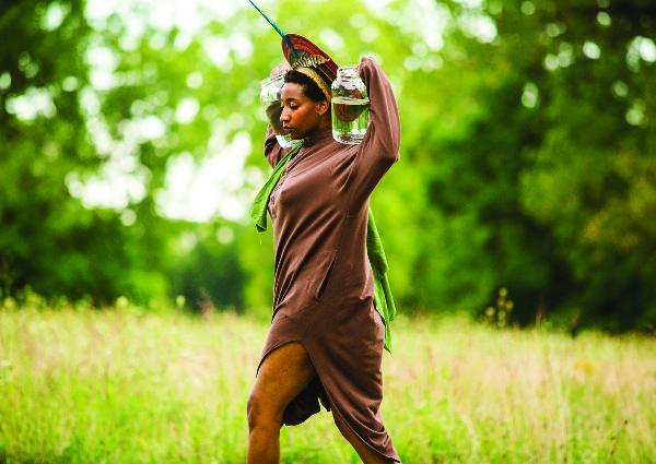 A person walking through a field with water jugs on their shoulders.