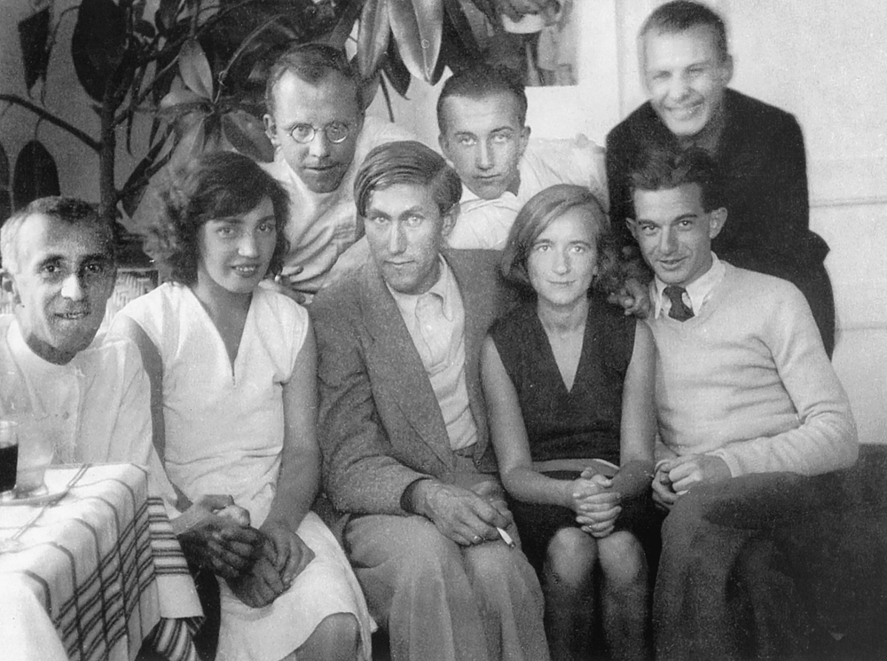 A group of eight individuals sitting closely together, all facing the camera, with some smiling.
