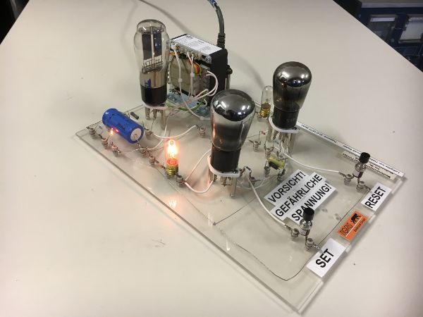 Large, trasparent circuit board with transistors, power adapter, wiring, and a light bulb that is illuminated.