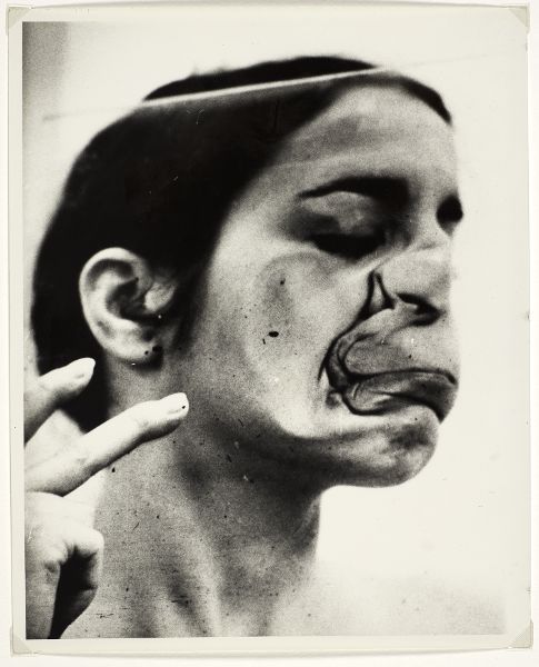 Woman pressing right side of her face firmly into glass from with indication she's moving forward as well, pinning her skin to the surface as she moves