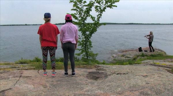 Two young bodies, wearing T-shirts and baseball caps, stretch out on a big boulder in a parallel line, head to foot, one face up and one face down.