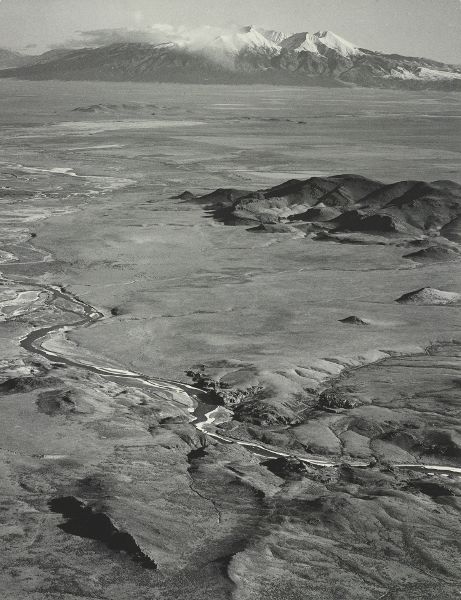An aerial view of a river in the foreground and snow-covered mountains on the horizon.