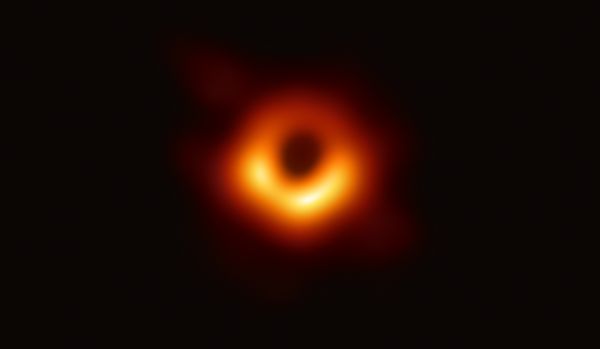 A scientific image of a black hole surrounded by colourful rim of yellow and red.