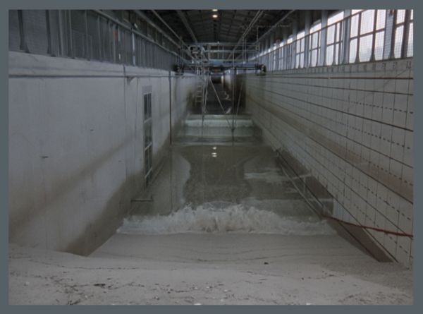Modeling water flows. Water flows down a gray hallway with scaffolding in the middle and walkways above either side.