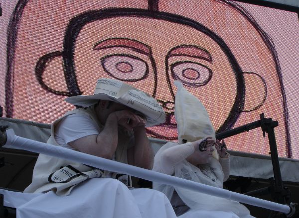 Two performers, dressed in white; in the background a video screen shows a cartoonish drawing of a human face.