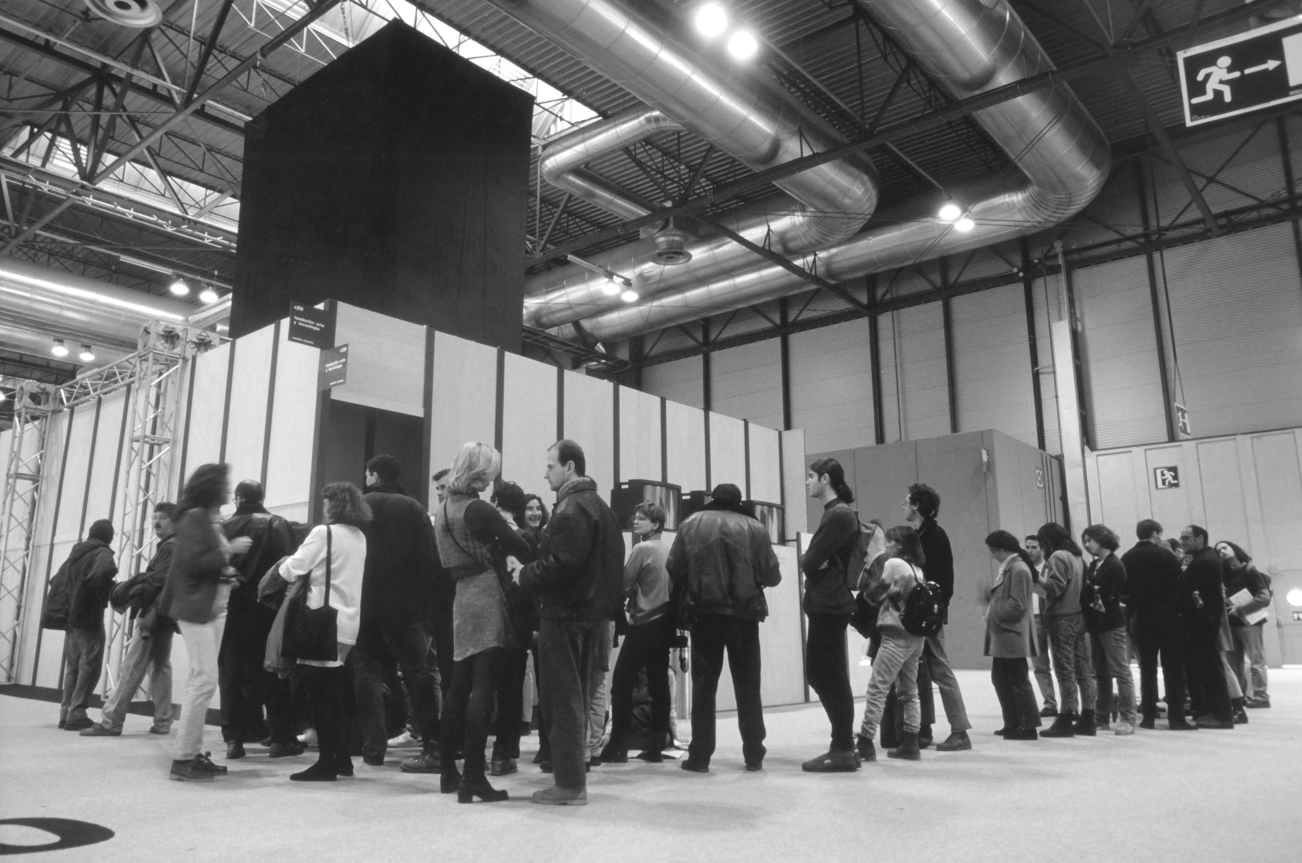 Image of audience members lining up in a large industrial space, waiting to enter a smaller room.