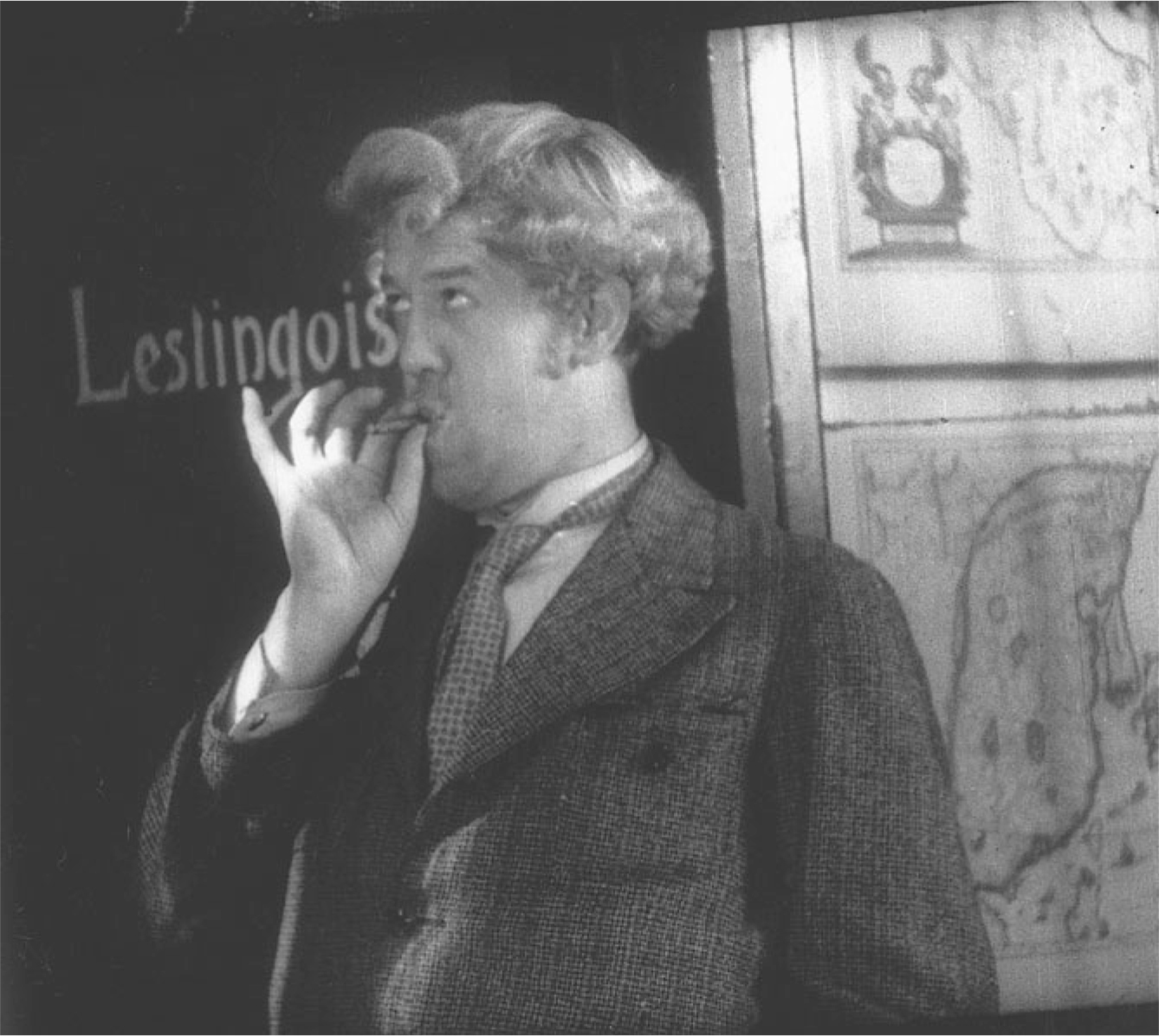 The exhibit displays a scene from “Boudu sauvé des eaux,” featuring Boudu positioned between the name of his benefactor and two maps from Blaeu's Atlas royal, while he is seen smoking a cigarette.