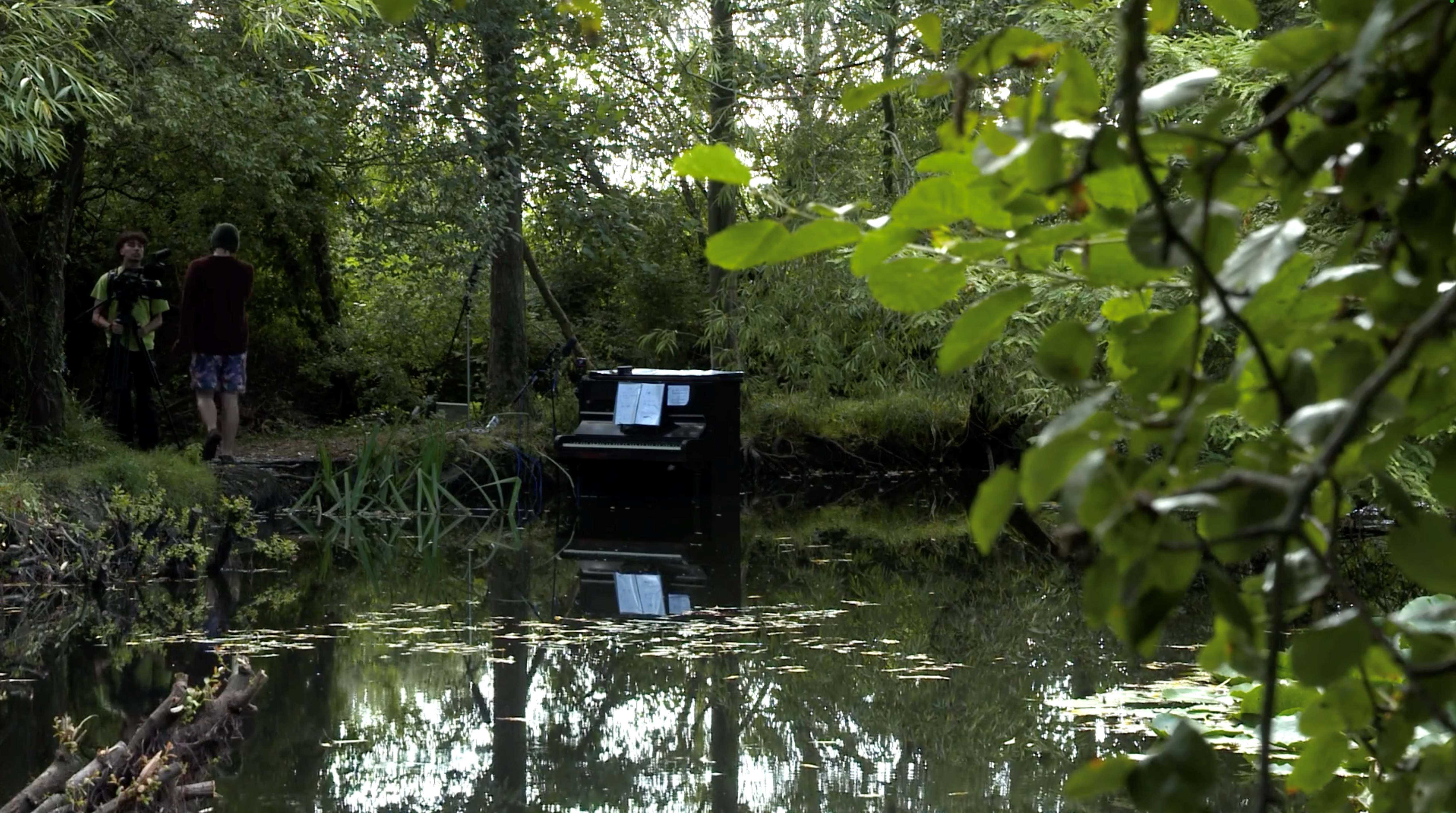 An upright piano in a pond, reflected upside-down in the water.