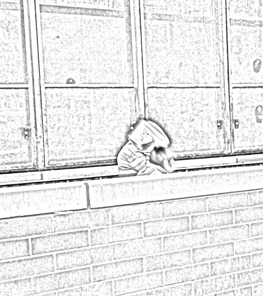 One student wearing a striped long-sleeve shirt covers his face with his notebook while his friend ducks behind a wall to hide from the camera.