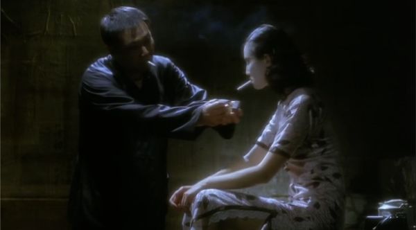 Mirroring the previous image, a woman sitting down is offered a light to her cigarette.