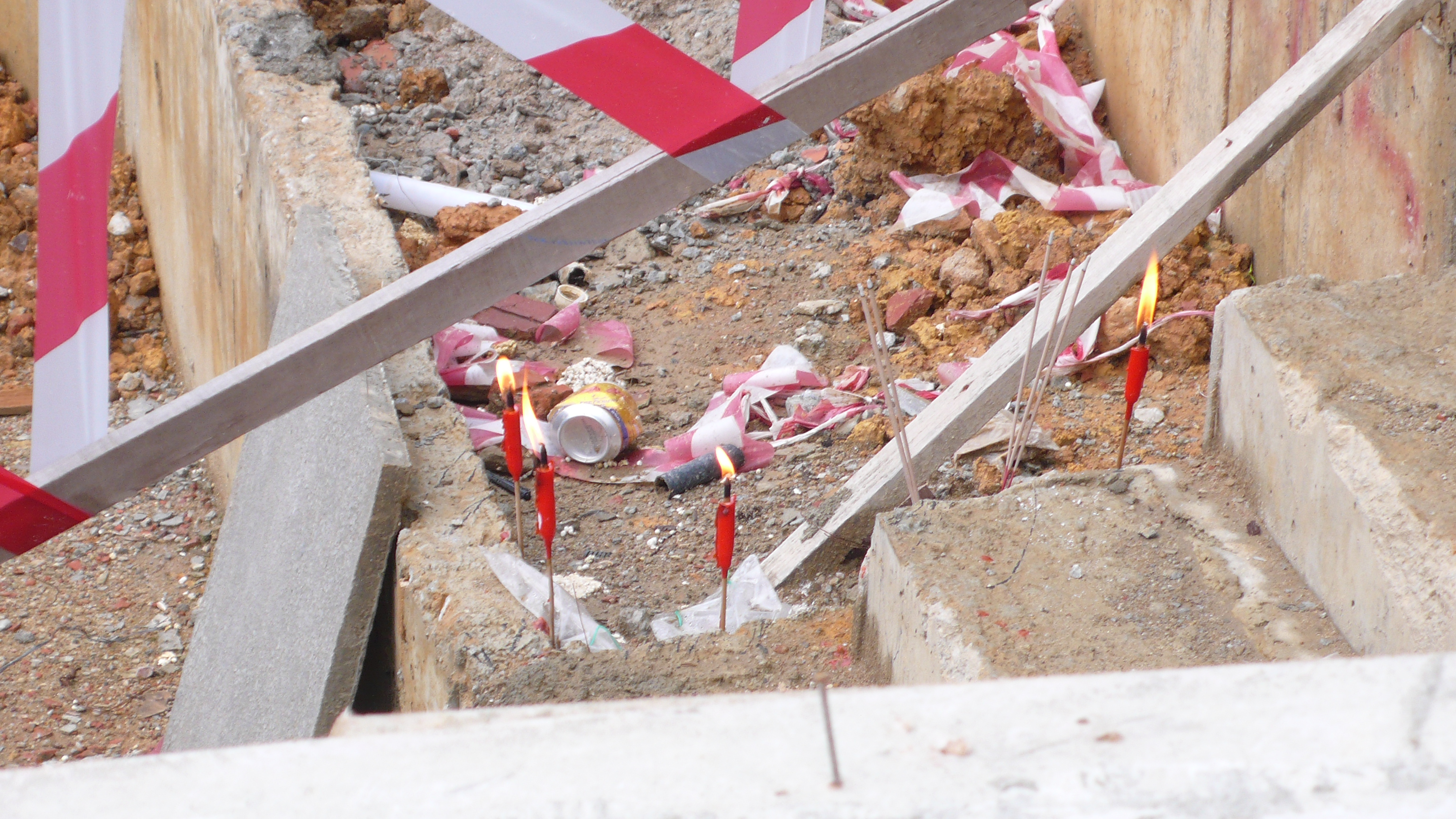 Burning candles and joss sticks line the edge of a half-constructed staircase. Construction waste and rubbish lie nearby.