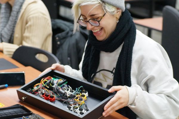 AJ, bedecked in a white sweatshirt and black scarf, holding an open black box with carefully arranged wiring.