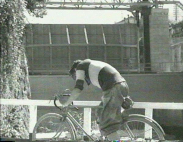 A man, dressed in striped bicycle-racing shirt, struggles to pedal his bicycle and keep up with the other racers.