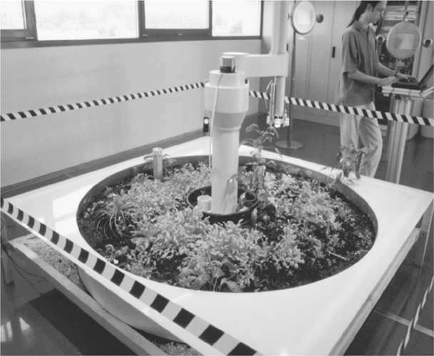 A photograph pf a miniature of a real garden with plants mounted on a table with a robotic equipment in the centre of the set up.