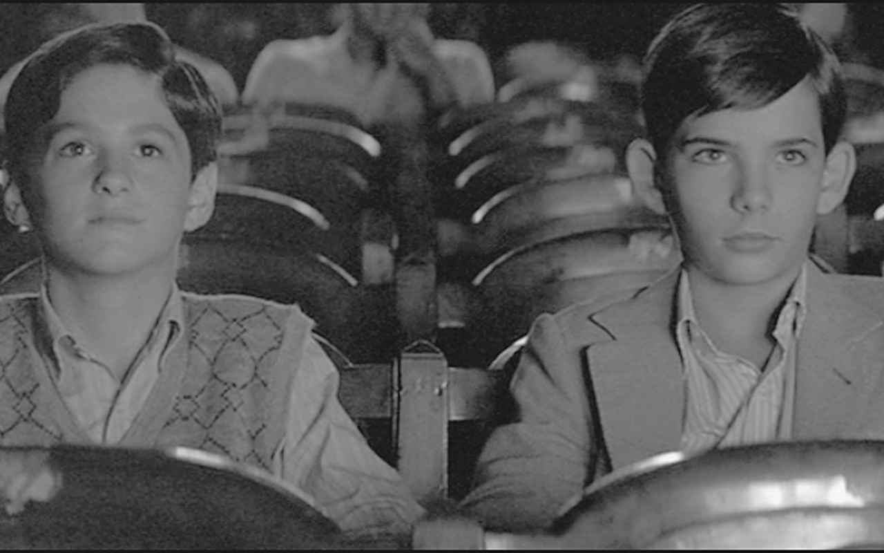 Two boys seated in a movie theater looking toward the screen.