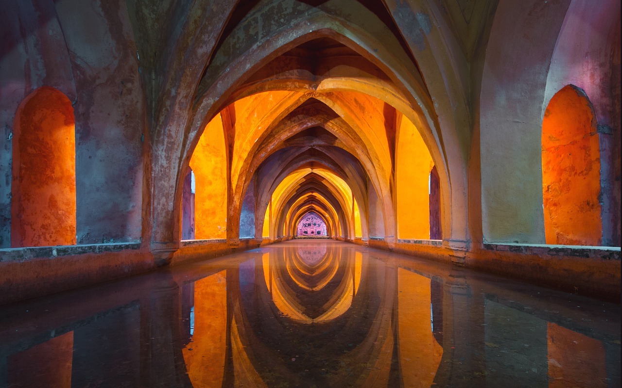 A shallow reflecting pool under concrete archways, known as the baths of Maria de Padilla.
