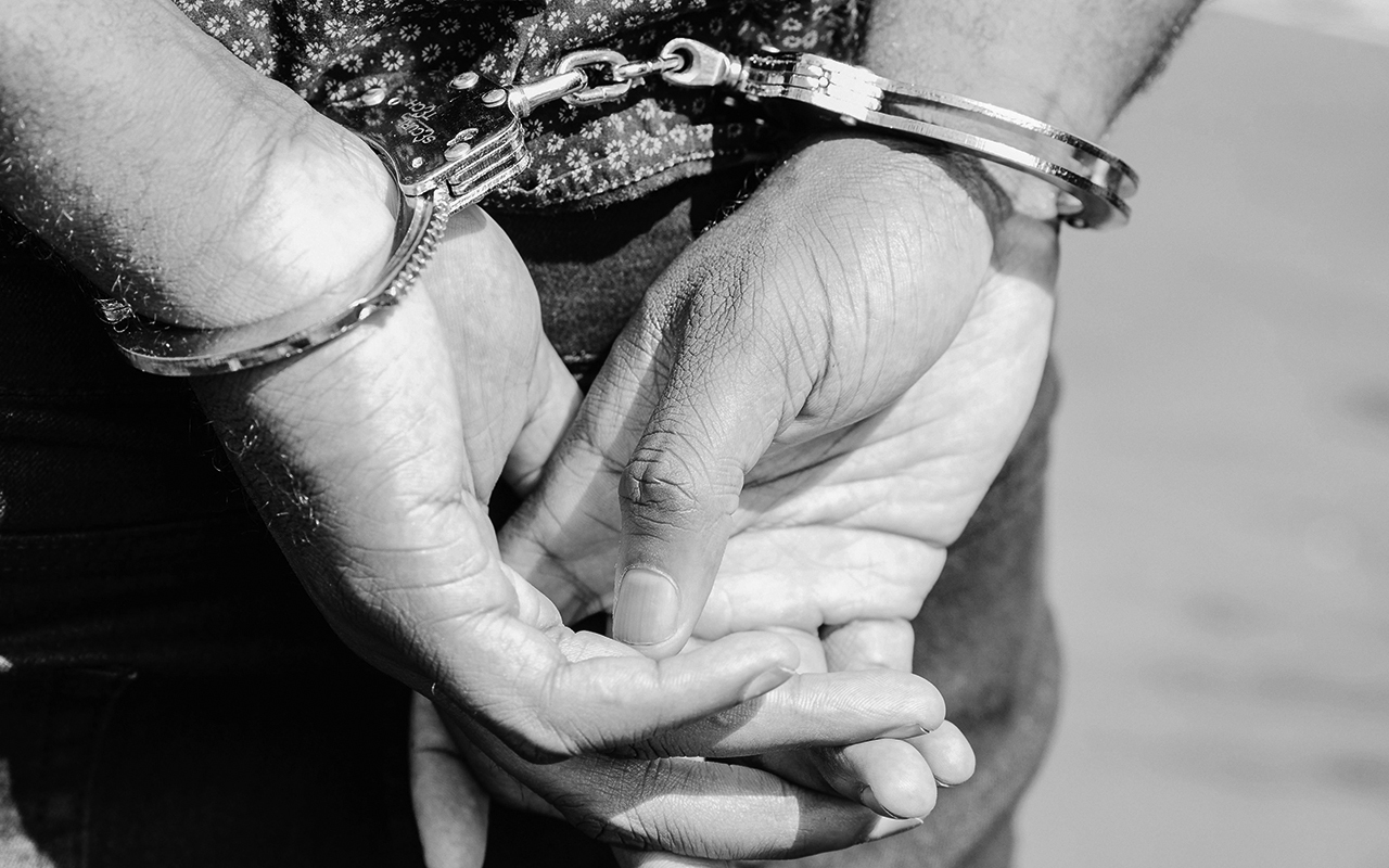 Closeup image of a black person’s hands behind their back in handcuffs.