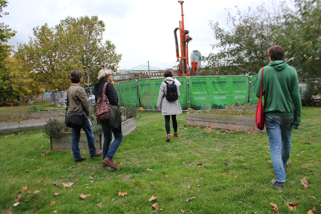 A group of four people walking through a green space to a position cordoned off by a temporary fence shielding a piece of heavy machinery.