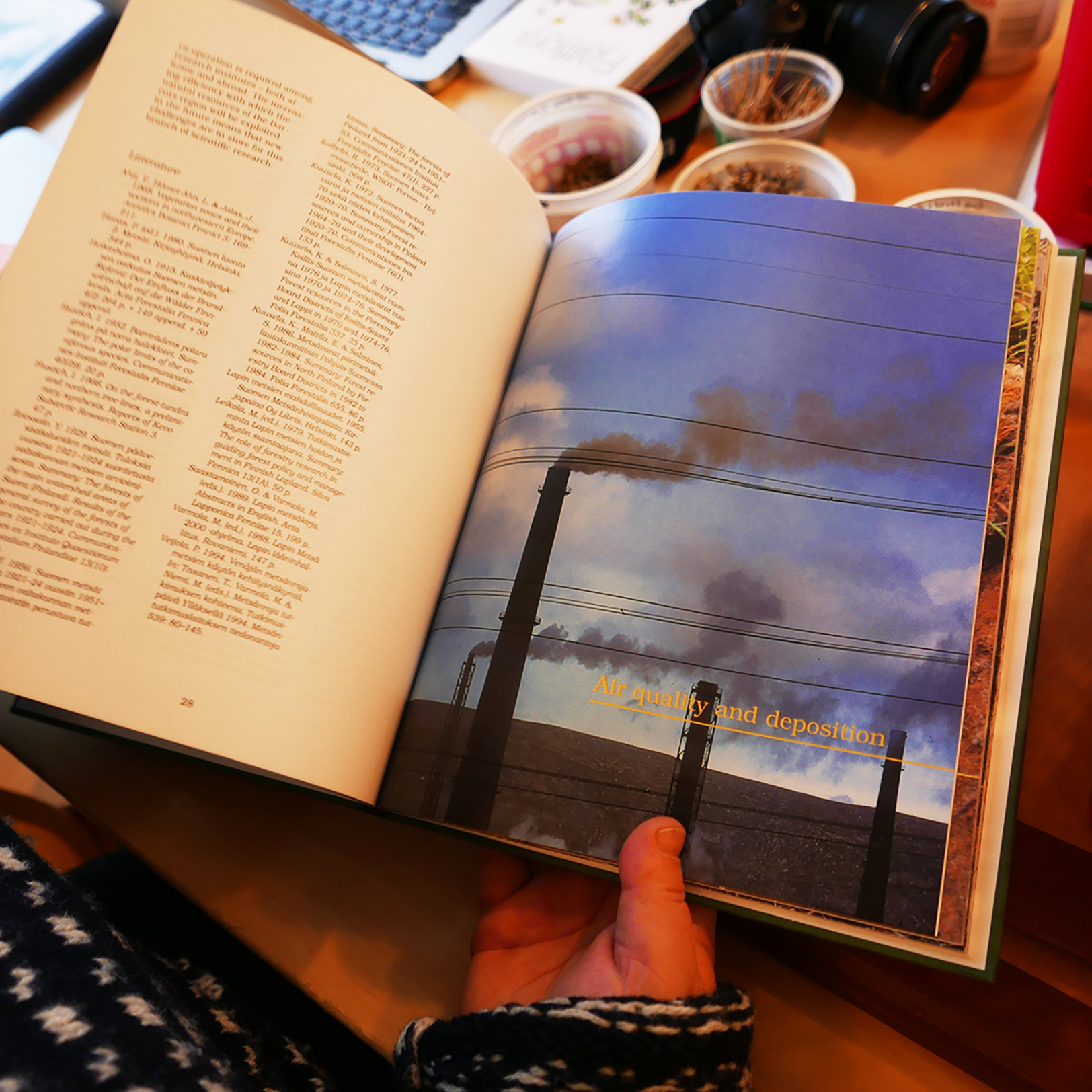 A person holding a book open to a part title that reads “Air quality and desposition” adorned with an image of smokestacks.