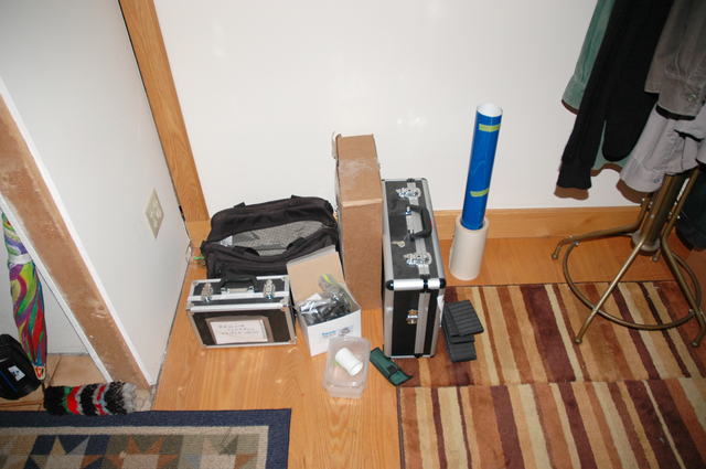 View looking down onto the floor of a residence with carrying cases, bags, a box, and assorted eqipment gathered in a corner.