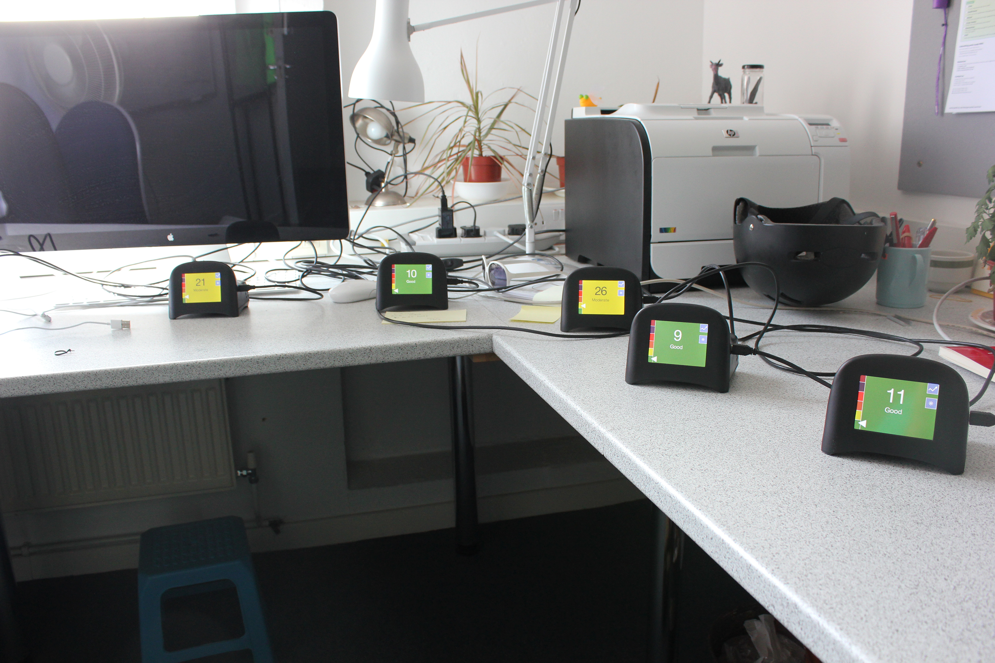 Five small digital displays sitting beside a desktop computer and printer showing different readouts ranging from 9—Good to 26—Moderate.
