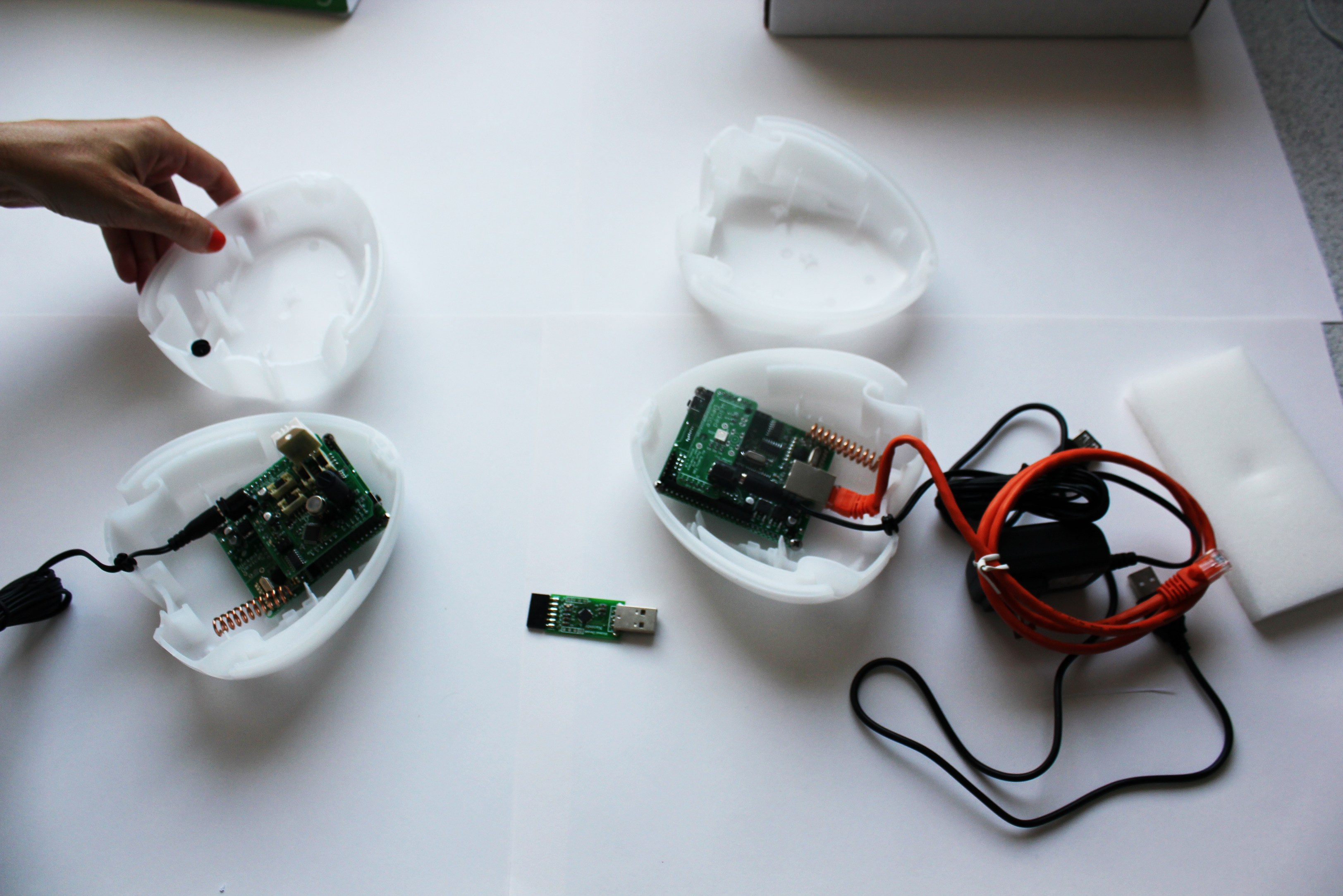 A pair of white, open casings revealing circuit boards and springs within. Both boards are connected to black USB cables. A CAT5 cable is also visible.