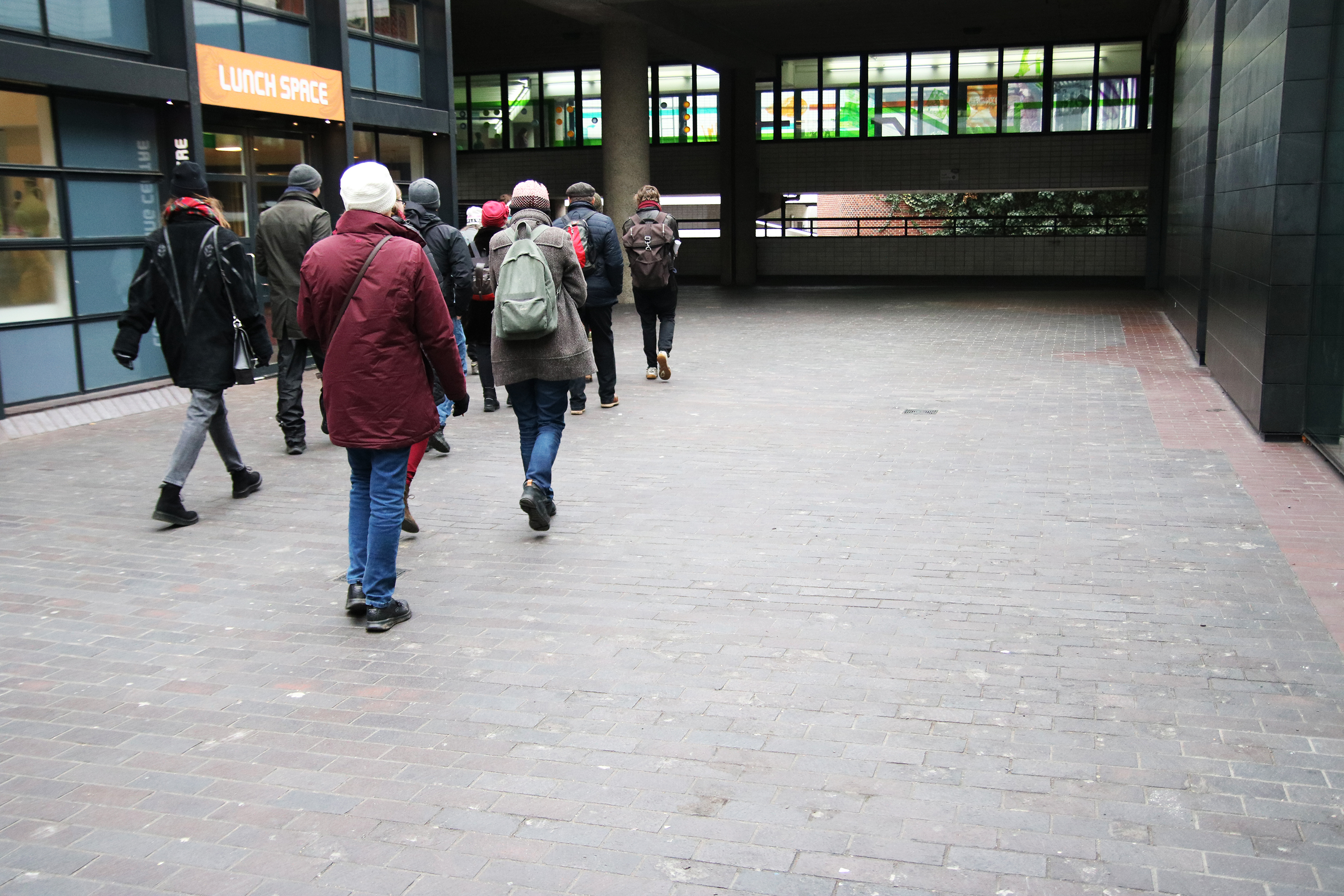 A small group of people in winter coats walking down a brick-paved street beside a lunch shop.